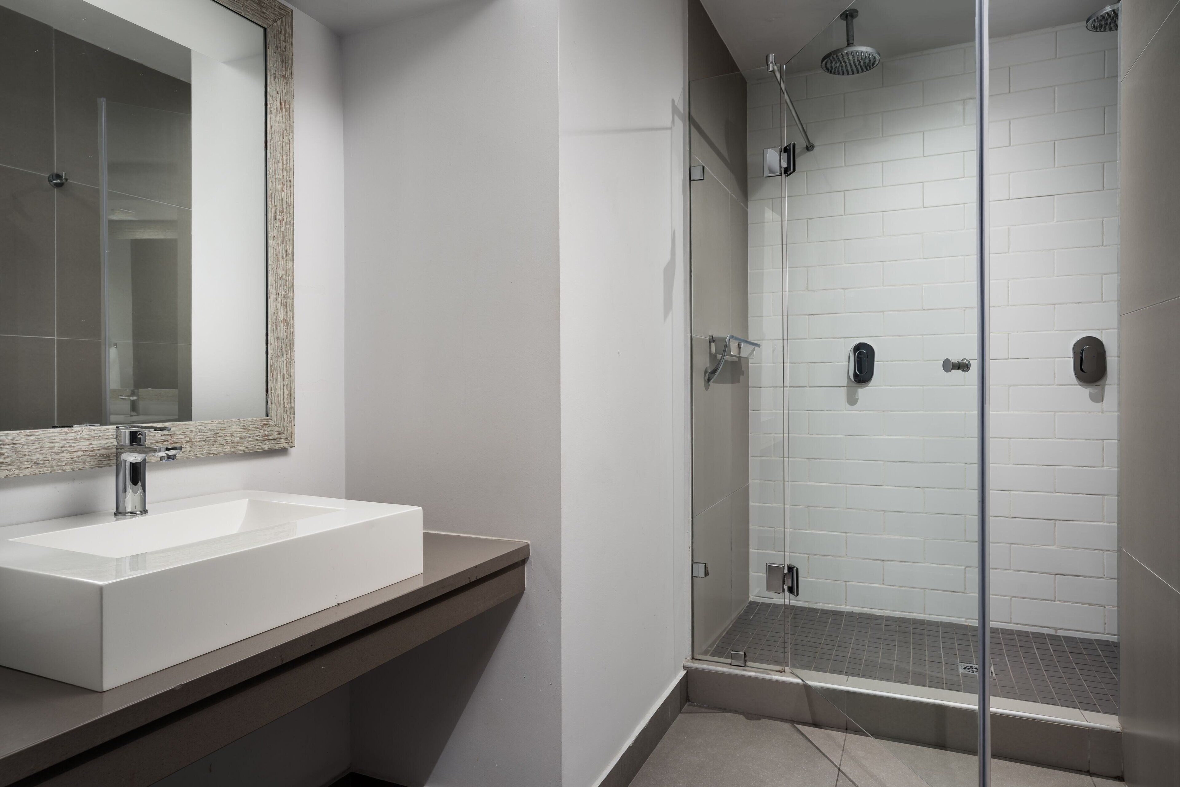 A modern bathroom with a white sink, a mirror, and a glass-enclosed shower area.
