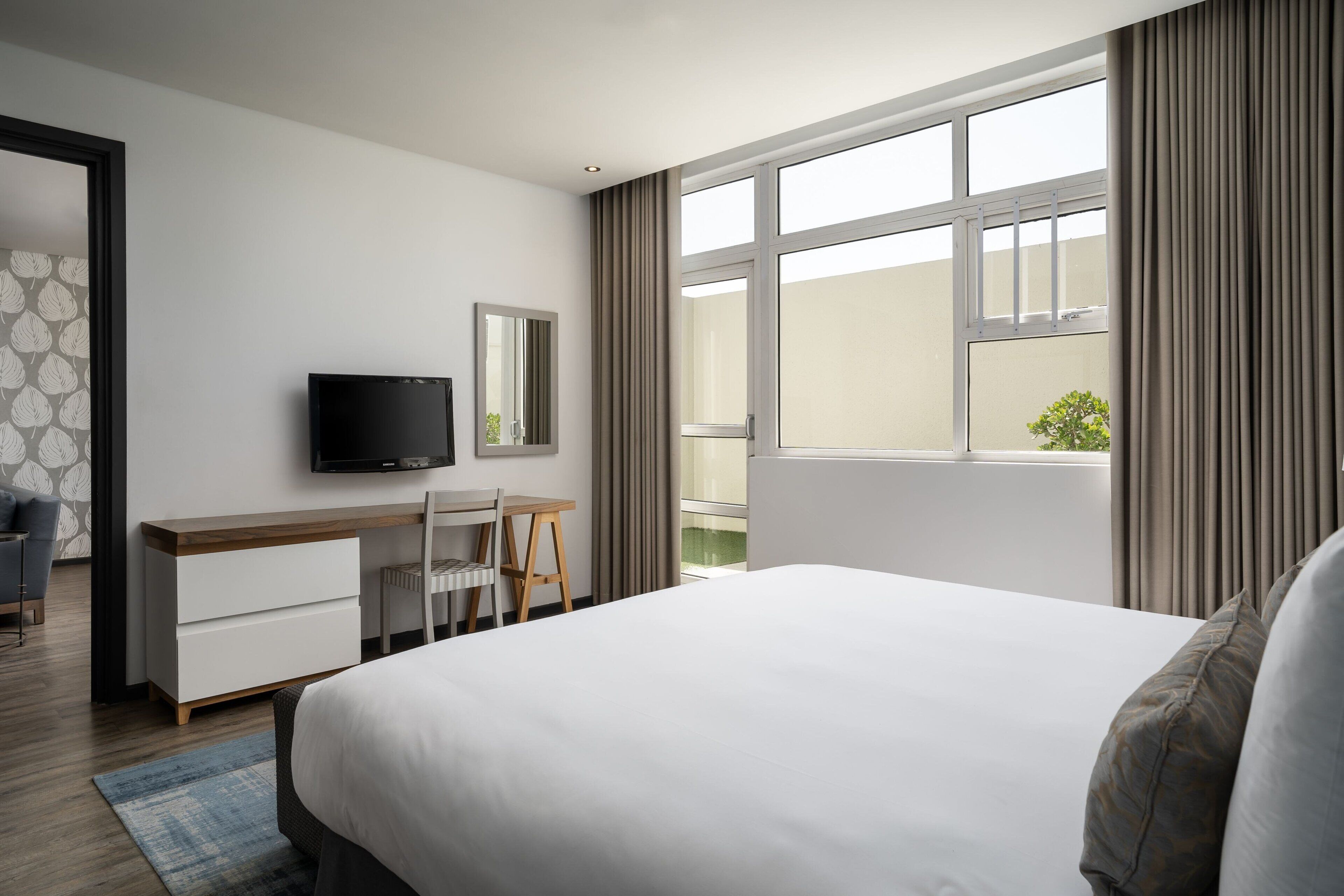 Une chambre d’hôtel avec un grand lit, un bureau avec une chaise, une télévision et une fenêtre avec des rideaux.