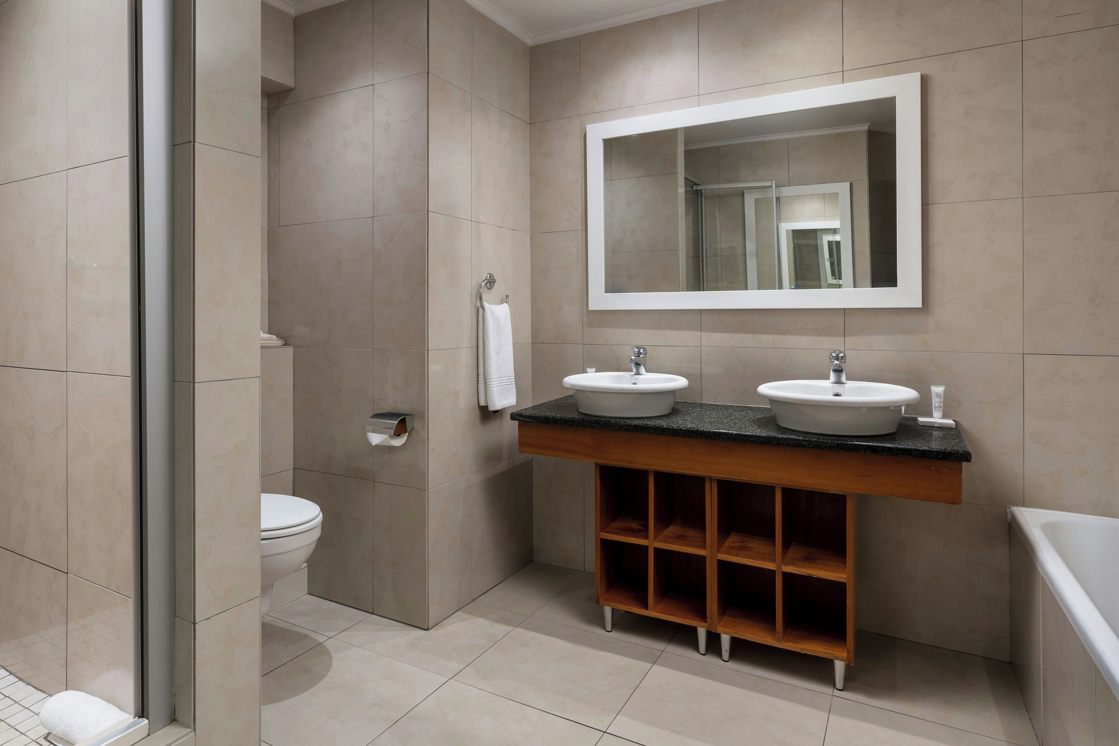 A modern bathroom with two sinks, a large mirror, and a shower area.
