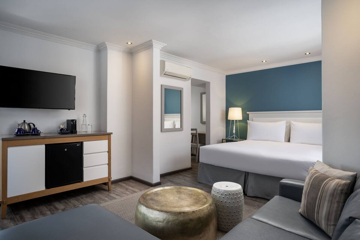 A hotel room with a bed, a desk with a computer, a television, and a small kitchenette.