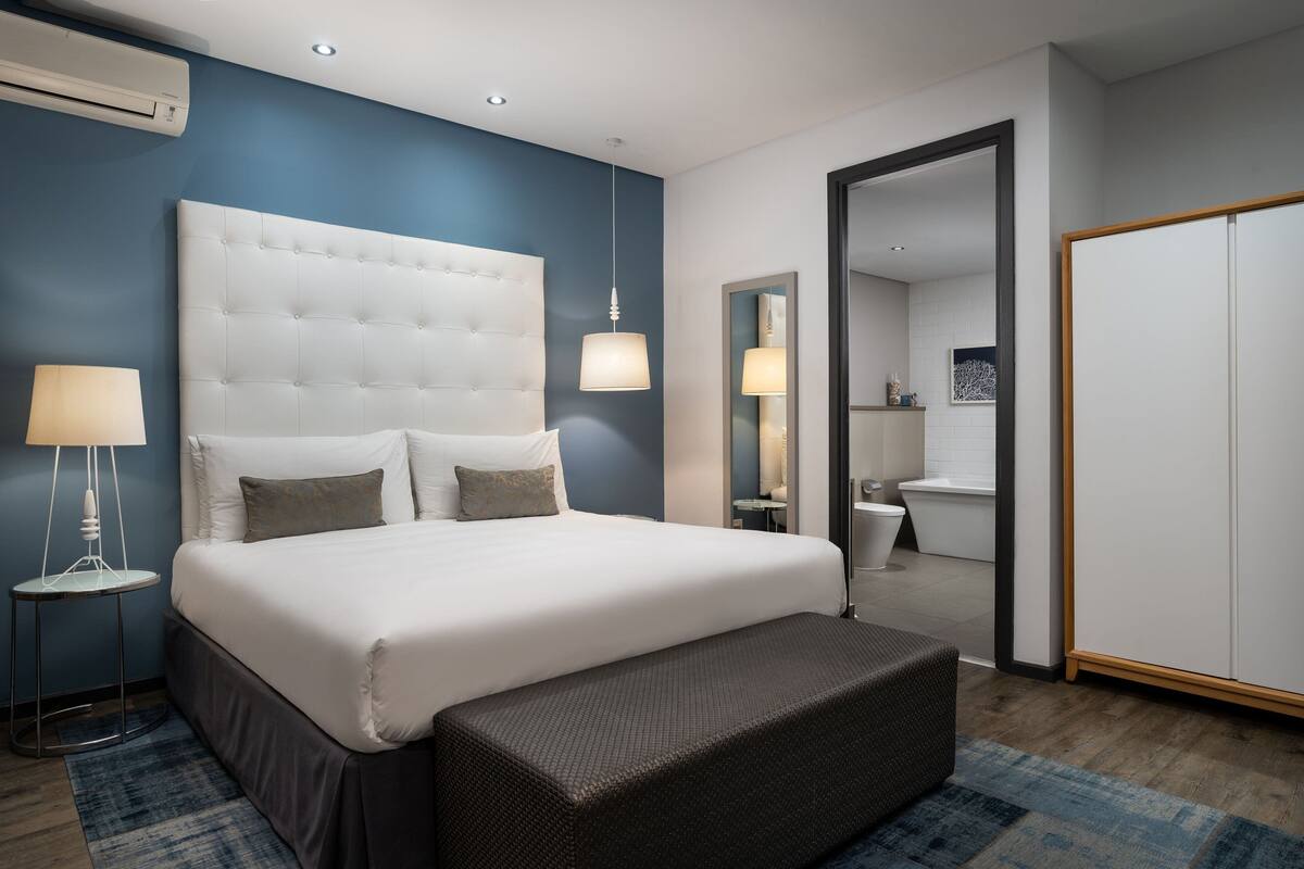 A modern hotel room with a large bed, bedside lamps, a mirror, and a wardrobe.