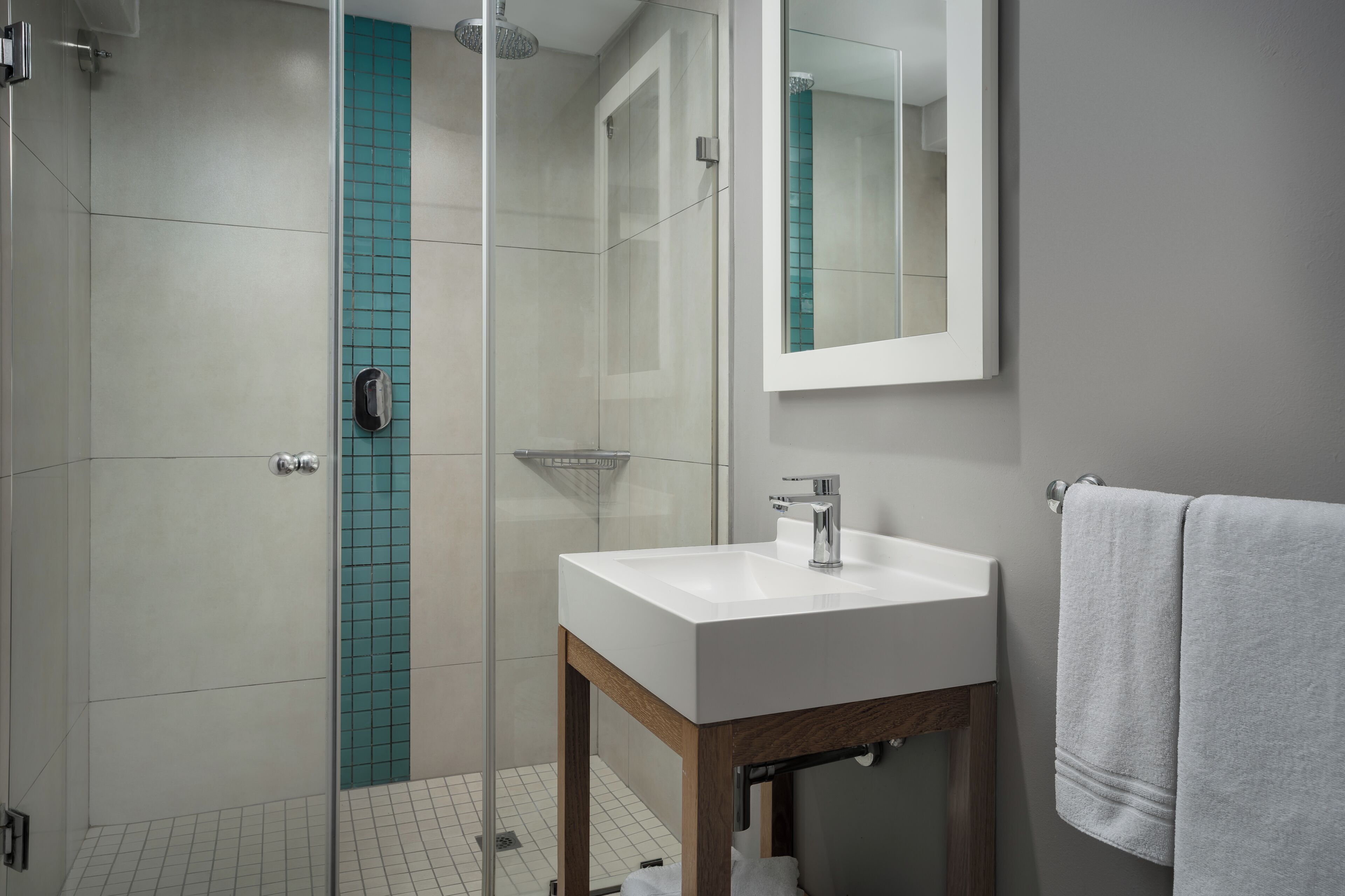 A modern bathroom with a glass shower enclosure, a white sink, and a wooden vanity.