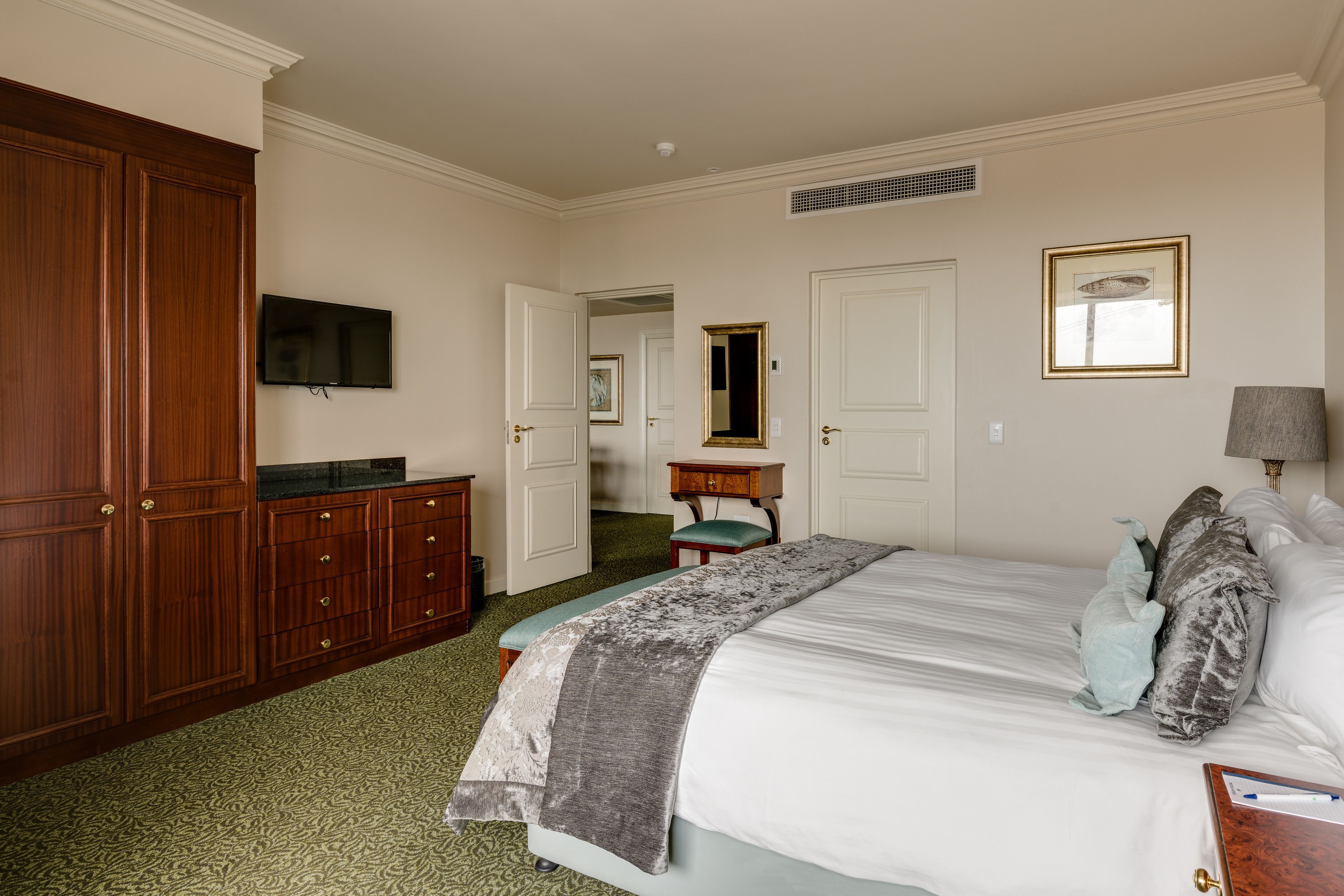 A bedroom with a large bed, a dresser, a television, a mirror, and a lamp.