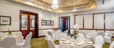 Un salón de banquetes con mesas redondas, sillas blancas y una araña de cristal.