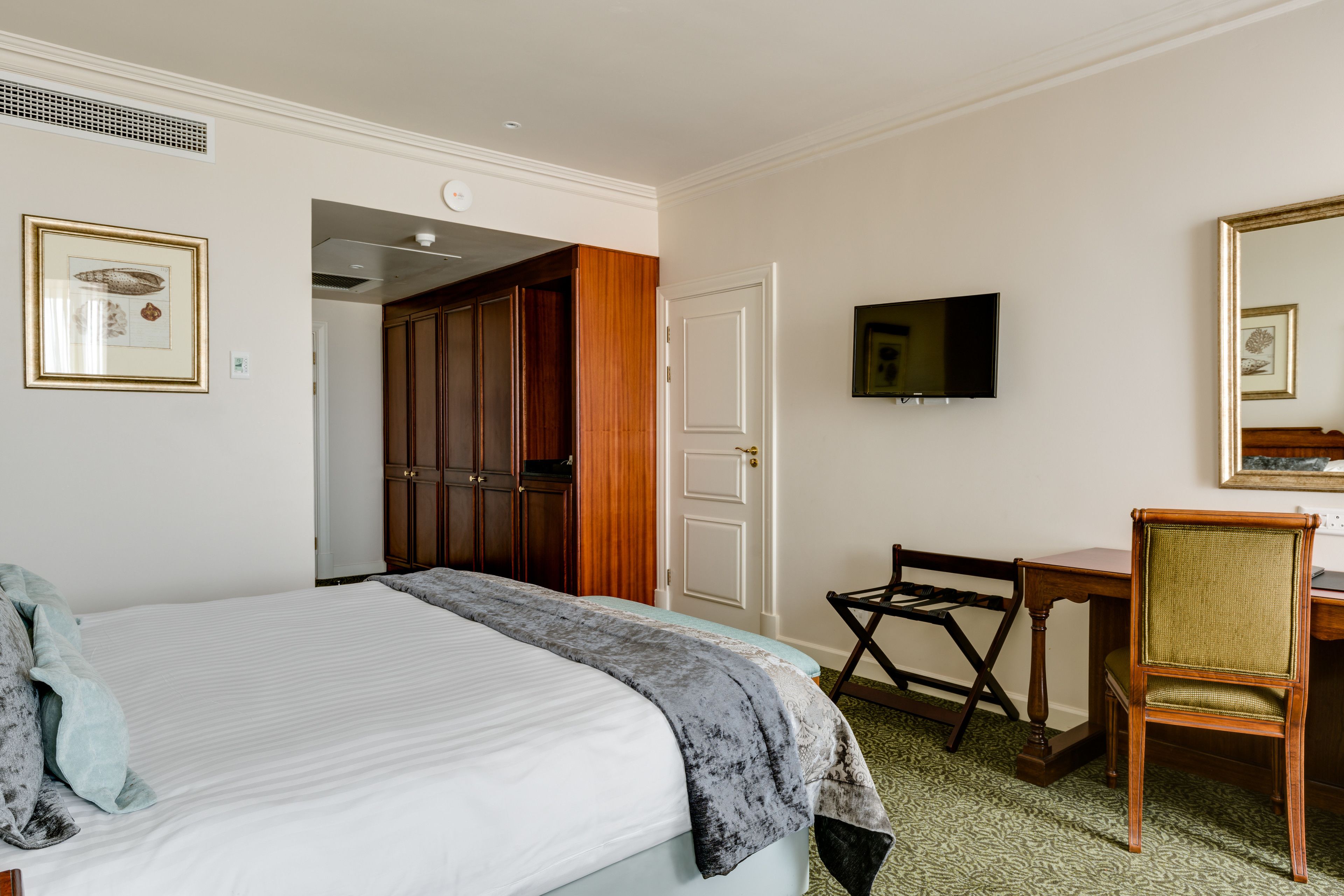 Une chambre d’hôtel avec un grand lit, un bureau, une chaise, une télévision et une armoire.