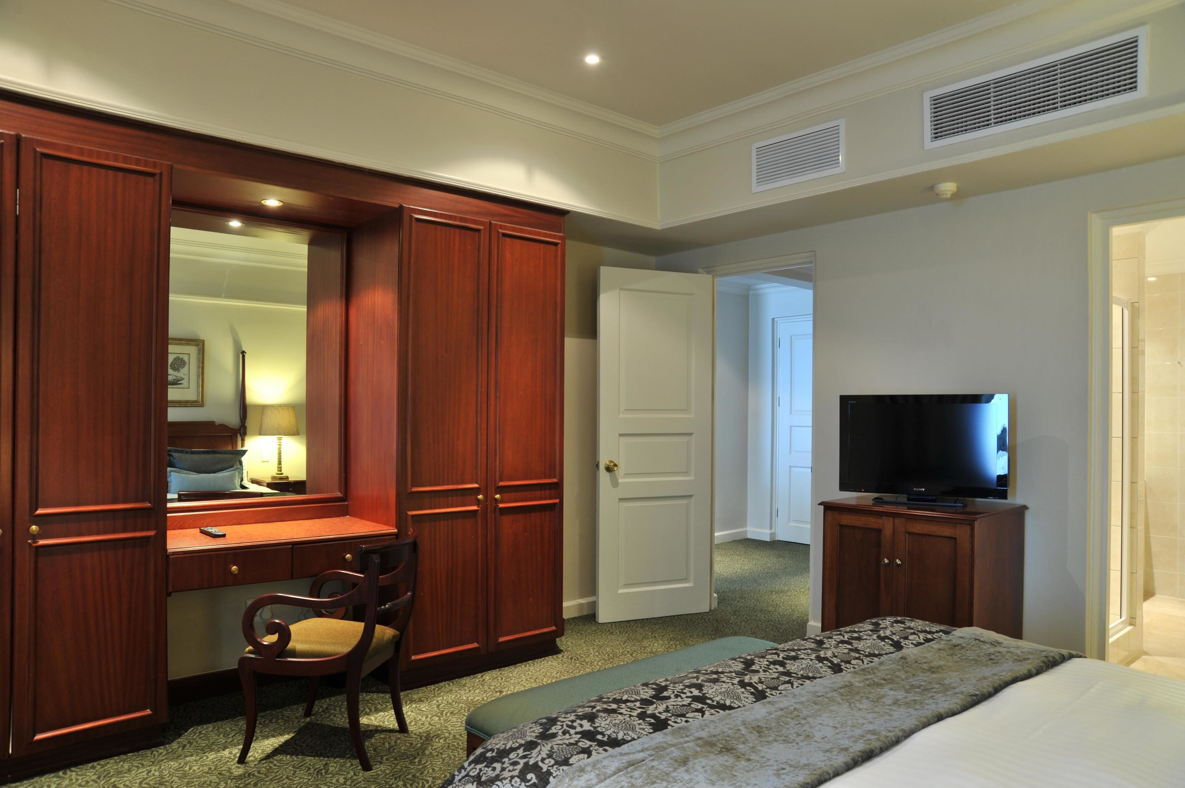 Habitación de hotel con escritorio de madera, silla, televisor y cama con colcha estampada.