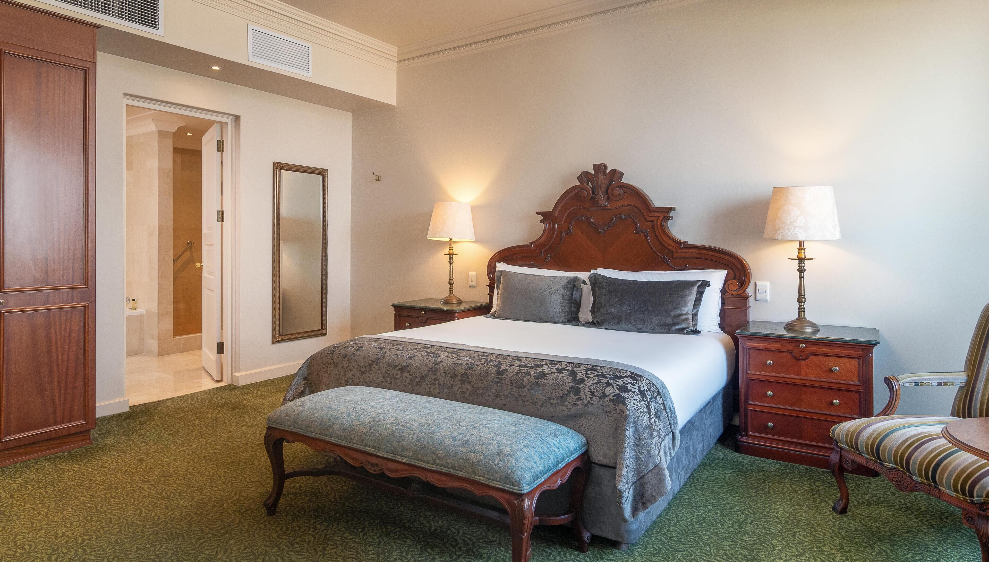 A neatly arranged bedroom with a bed, two bedside tables with lamps, a chair, and a bench.
