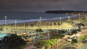 A beachside view with a road, palm trees, and a distant hill with a lighthouse. - The Edward Hotel (Durban)