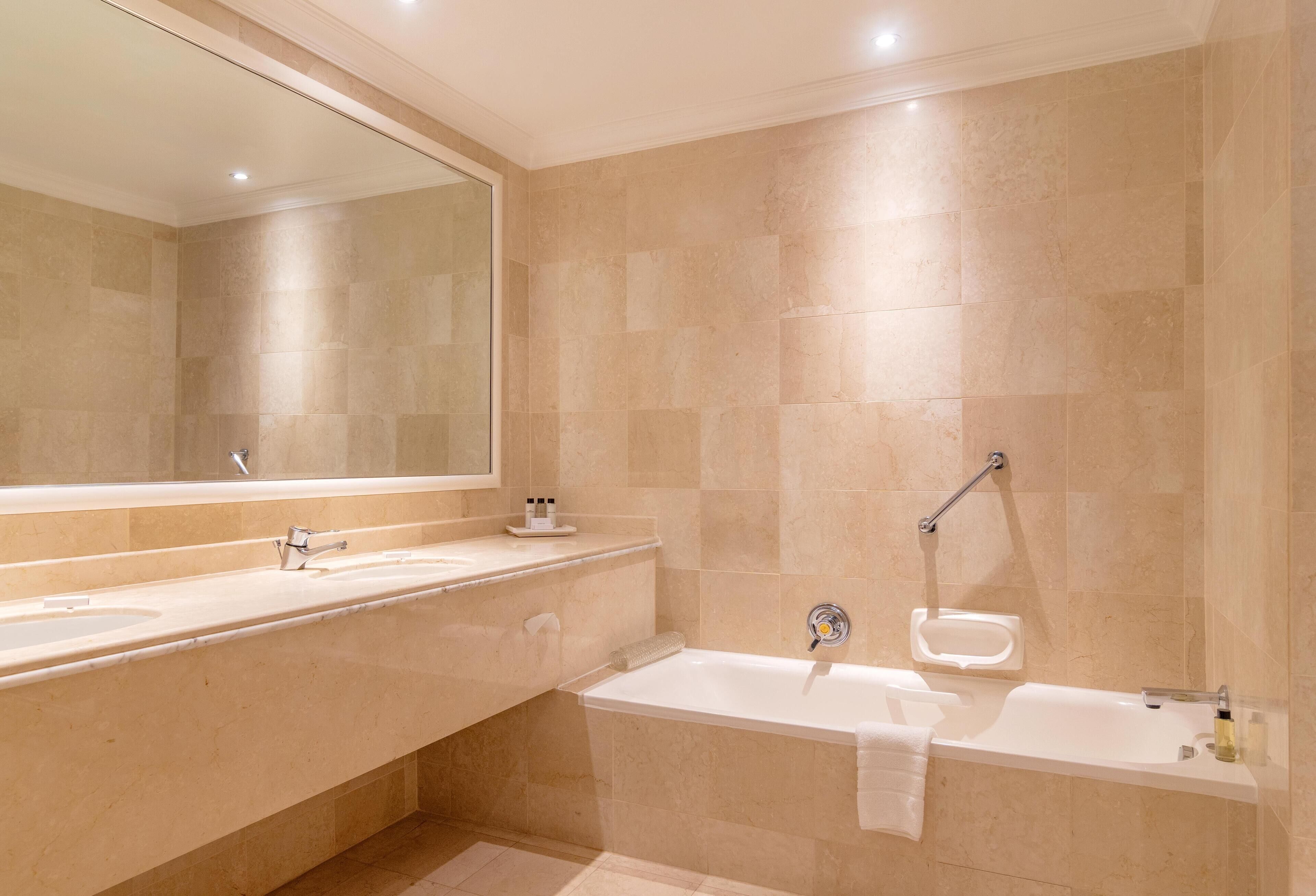 Un baño moderno con un espejo grande, dos lavamanos, una bañera y una ducha.