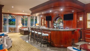 A bar area with a wooden bar counter, multiple bar stools, and a television screen. - The Edward Hotel (Durban)