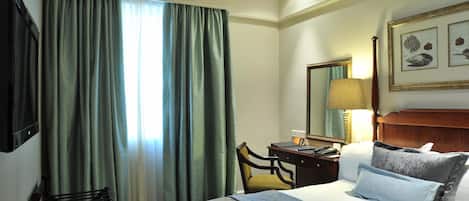 A hotel room with a bed, a desk, a chair, a lamp, and a large mirror.
