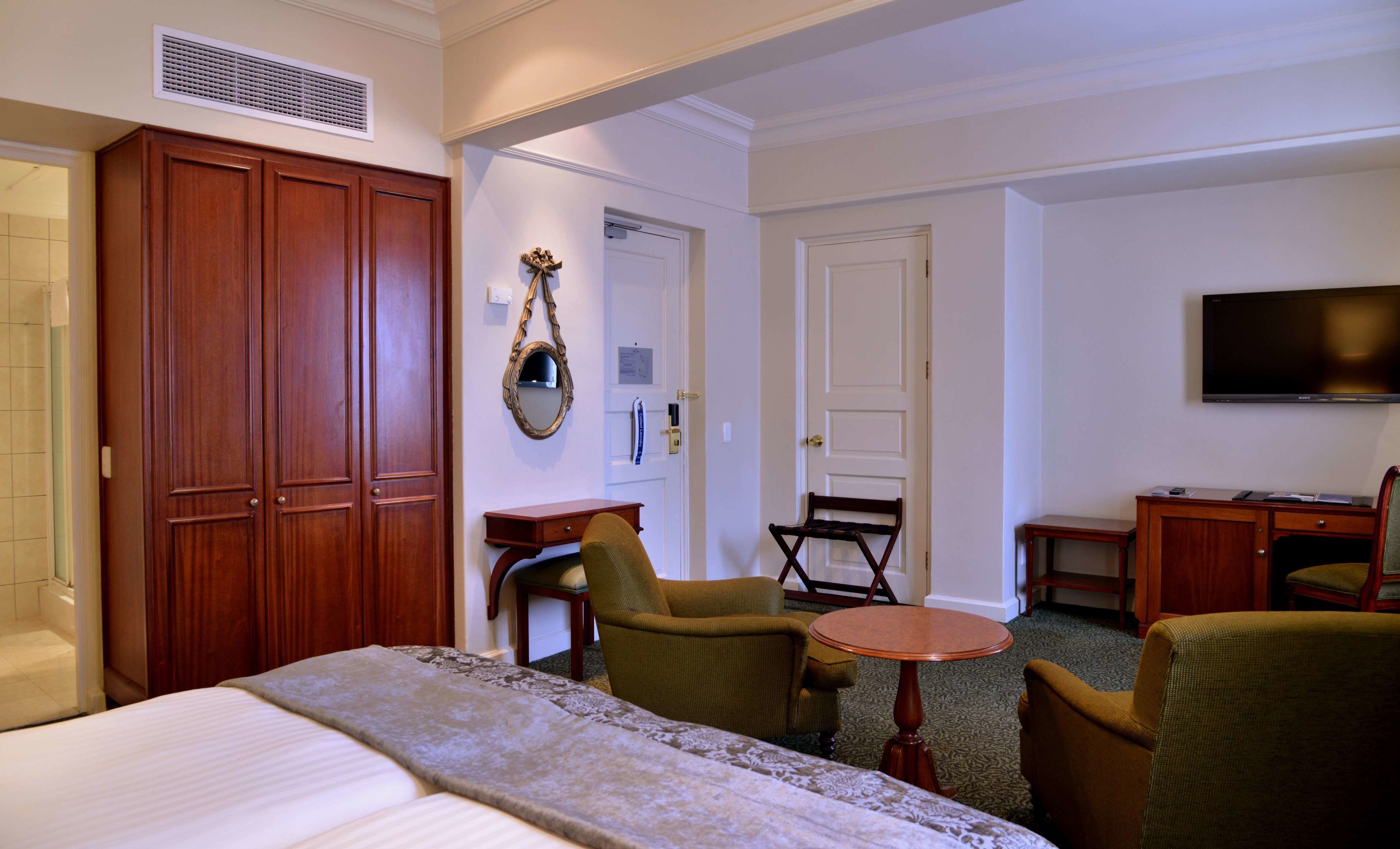 A hotel room with a bed, two armchairs, a small table, a desk with a chair, a television, and a wardrobe.