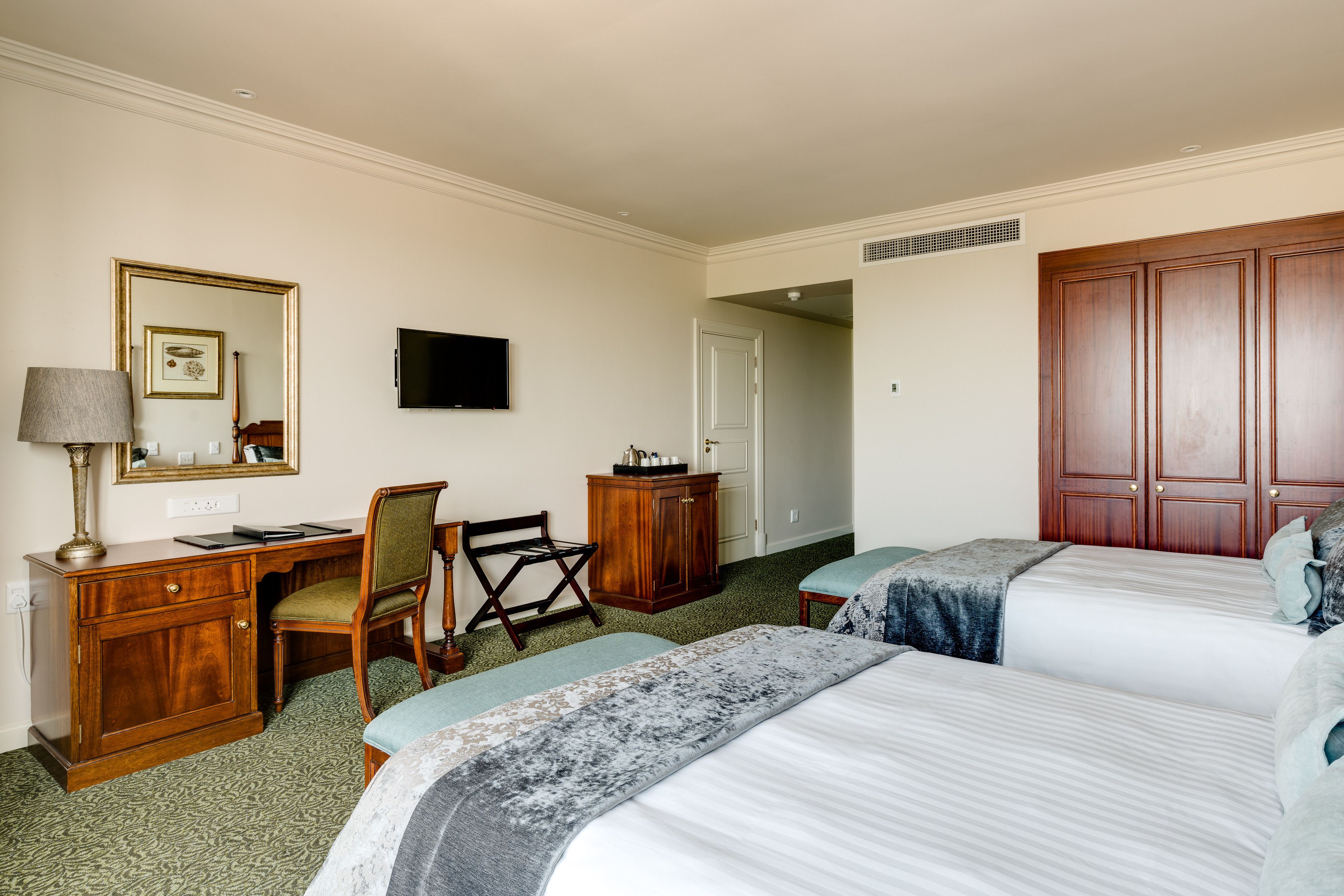 Habitación de hotel con dos camas, un escritorio, una silla, un televisor y un armario.