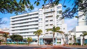 A multi-story hotel with a modern design, featuring balconies on each floor, a prominent entrance with a sign, and palm trees in the foreground. - The Edward Hotel (Durban)