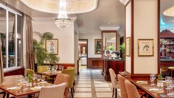 A hotel dining area with tables set for guests, a bar in the background, and a view of the pool through the window.
