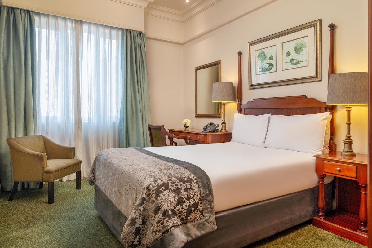 Una habitación de hotel con una cama grande, una silla, un escritorio, una lámpara y un espejo.