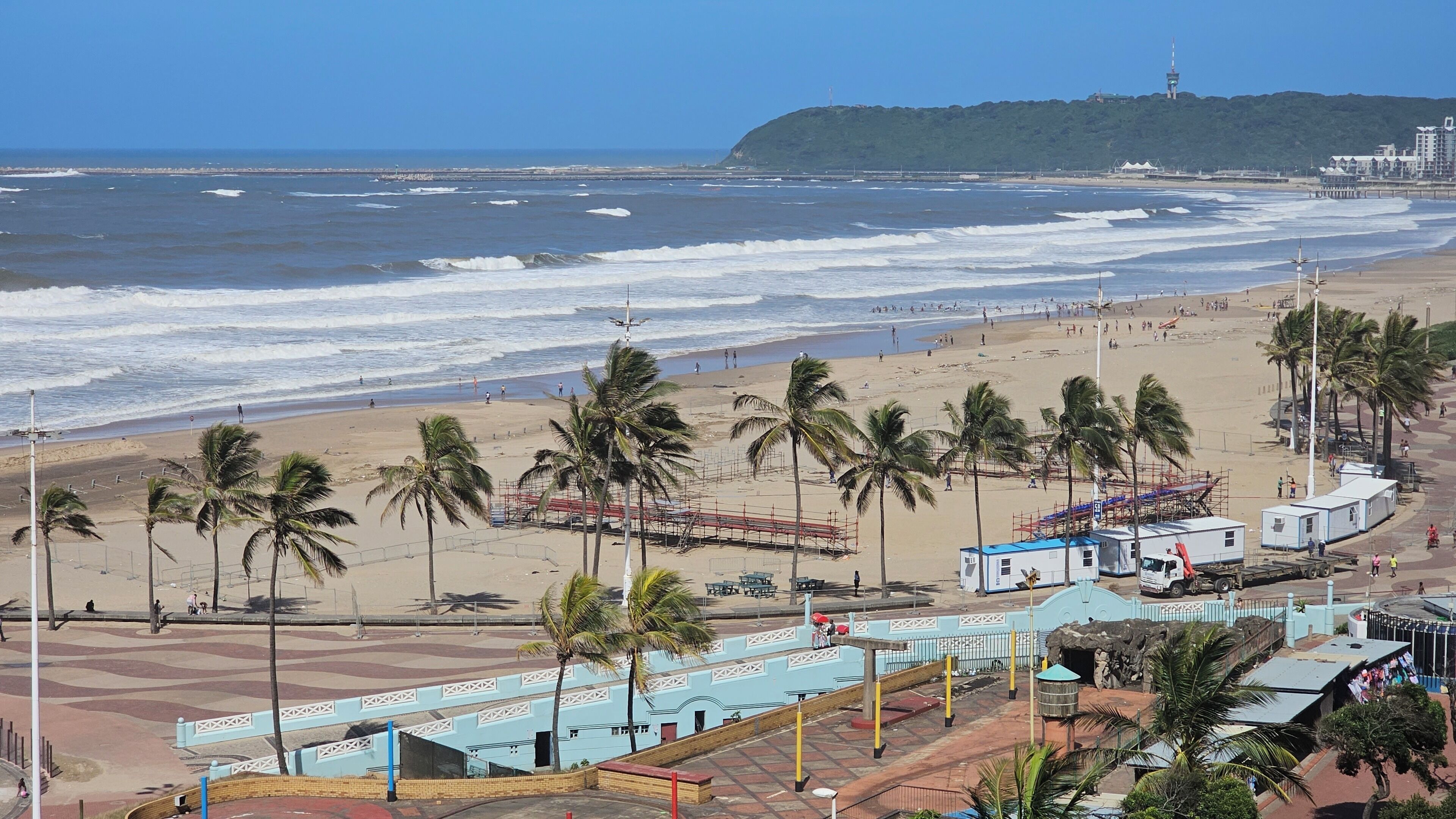 A beach with palm trees, a pier, and a building with a blue roof.