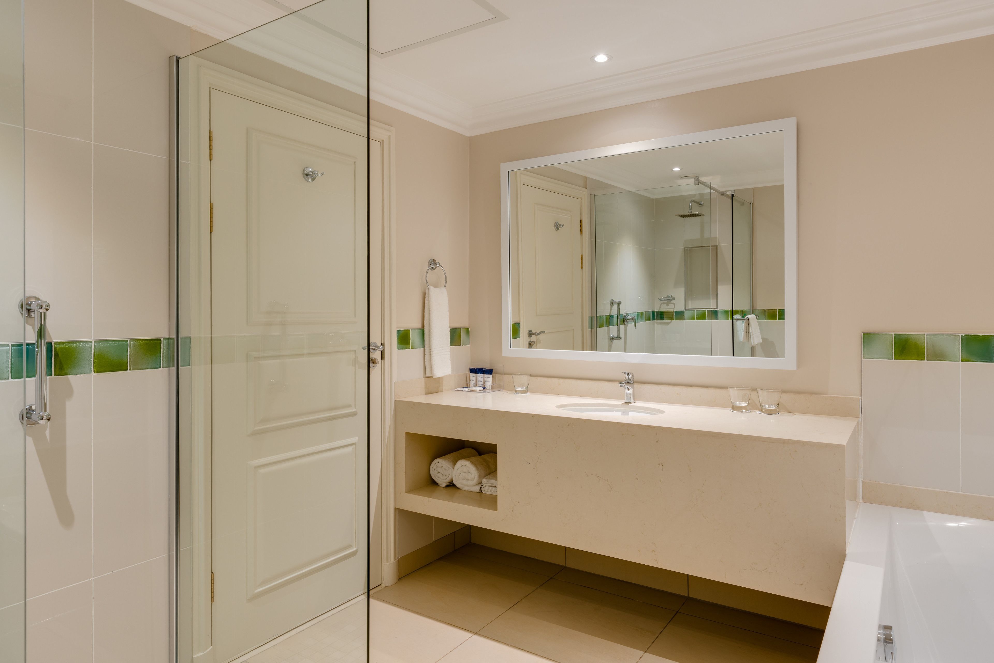 A modern bathroom with a glass shower enclosure, a large mirror, and a beige vanity with a sink and countertop.