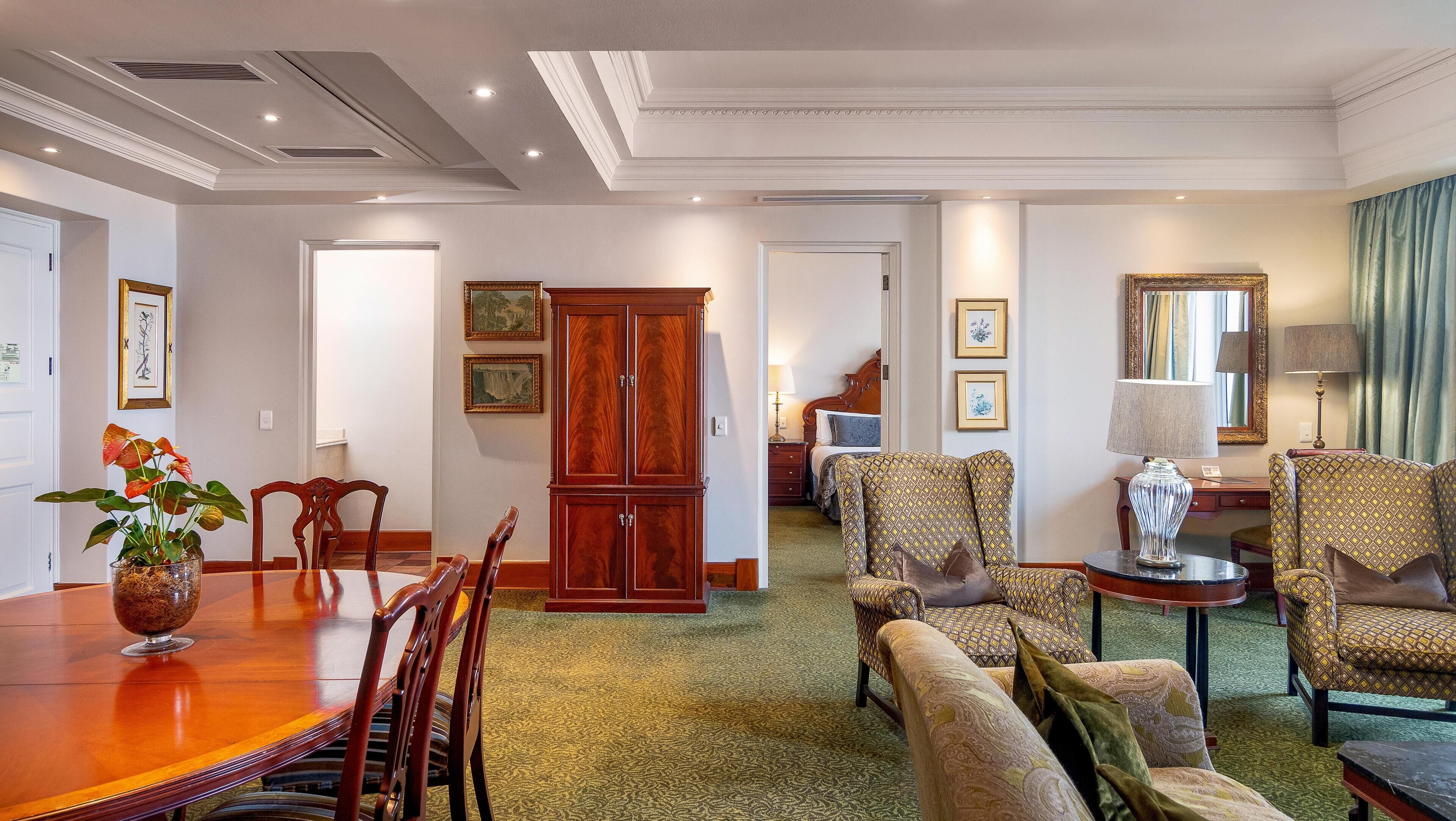 A spacious living area with a dining table, chairs, a sofa set, and a large wooden cabinet.