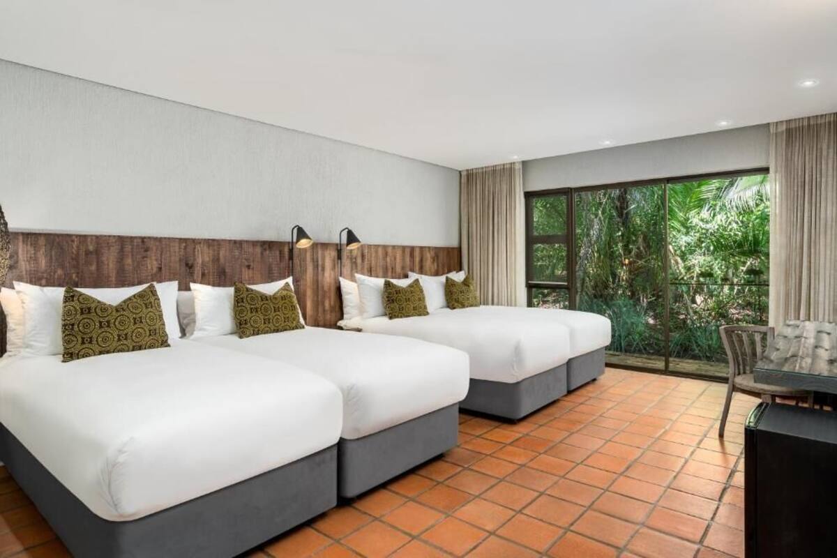 A hotel room with two beds, a TV, and a large window with a view of greenery.