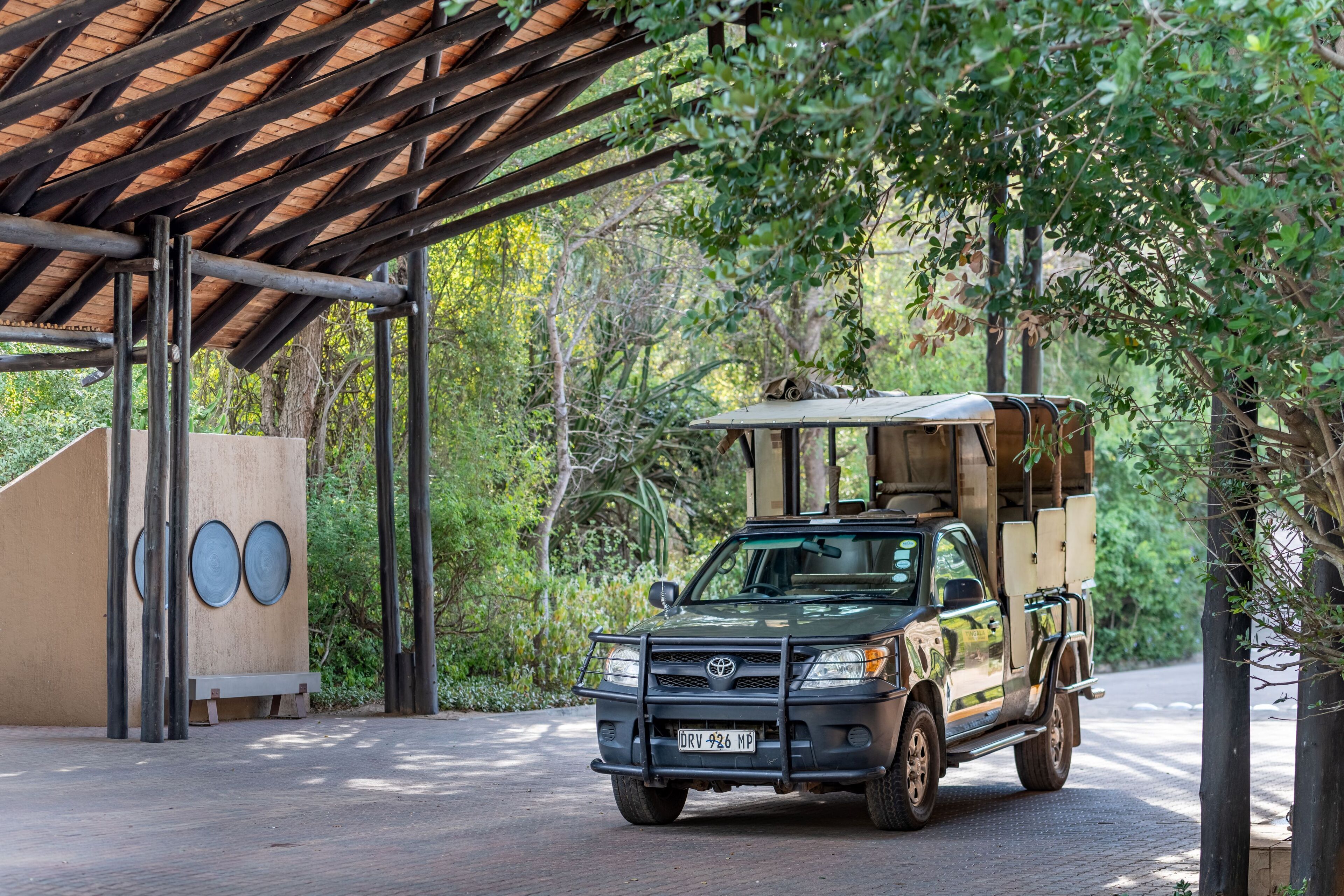 A Toyota Land Cruiser parked under a wooden shelter with a natural backdrop.