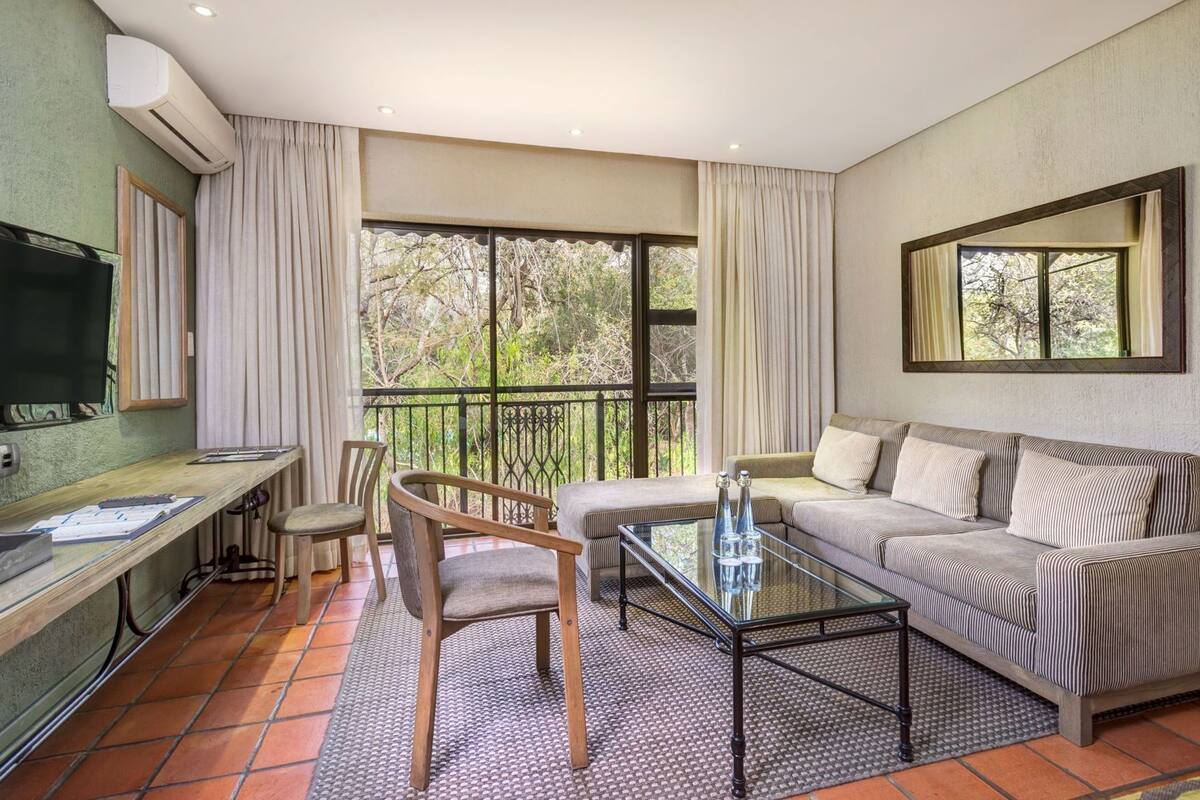 A living room with a sofa, a coffee table, a TV, and a balcony with curtains.