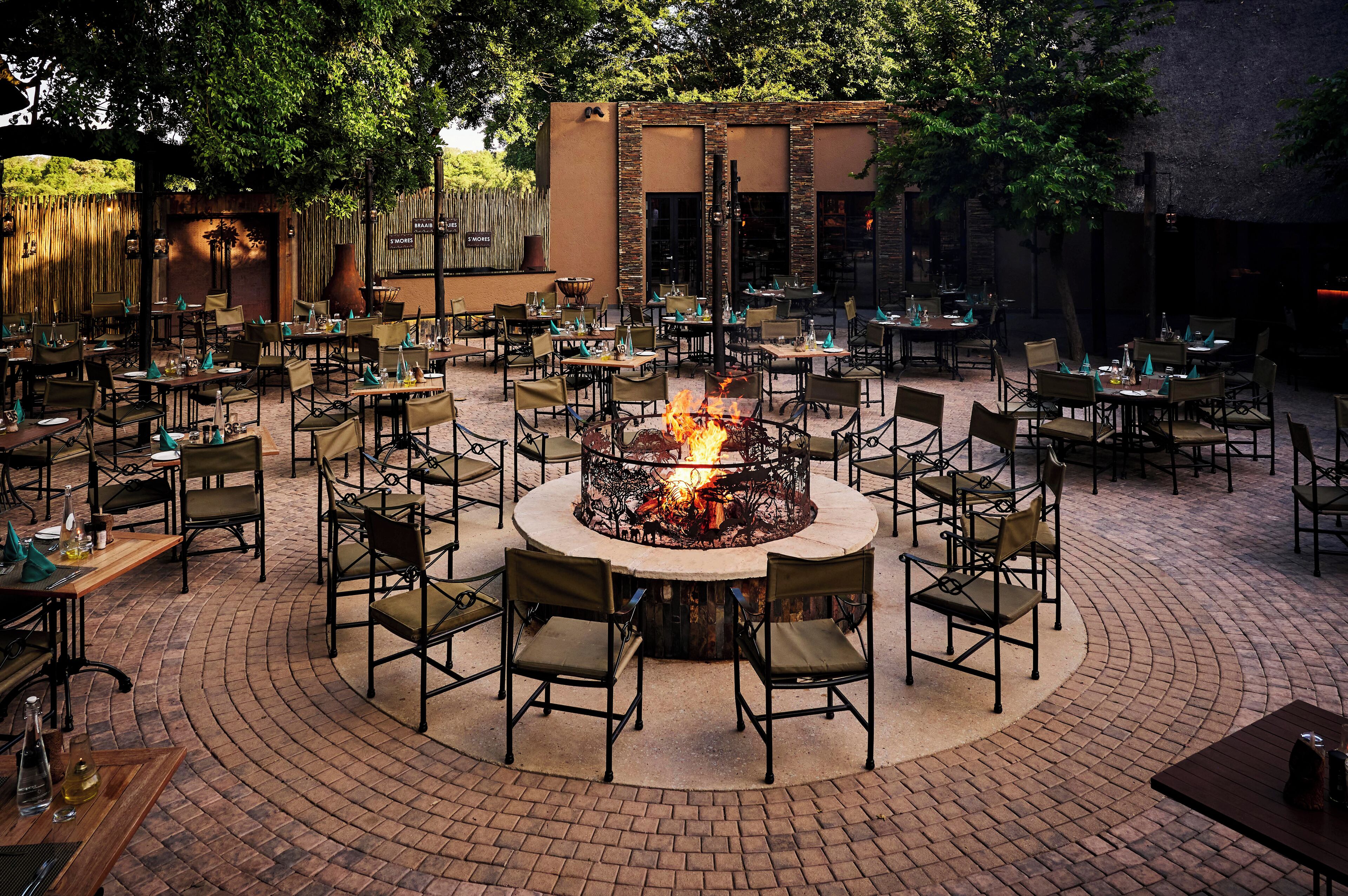 An outdoor dining area with a central fire pit surrounded by tables and chairs.