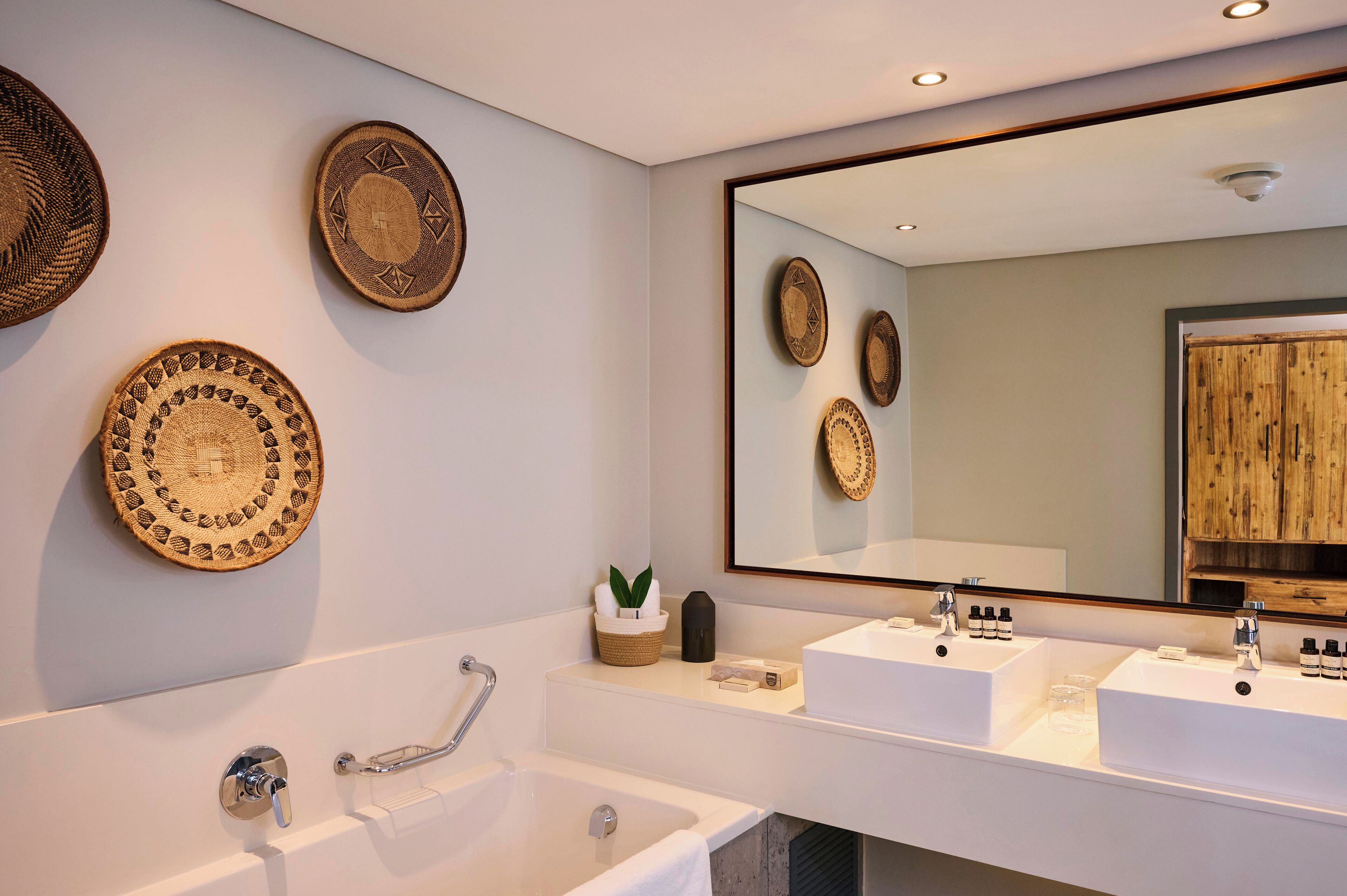 A modern bathroom with a large mirror, two sinks, and decorative woven plates on the wall.