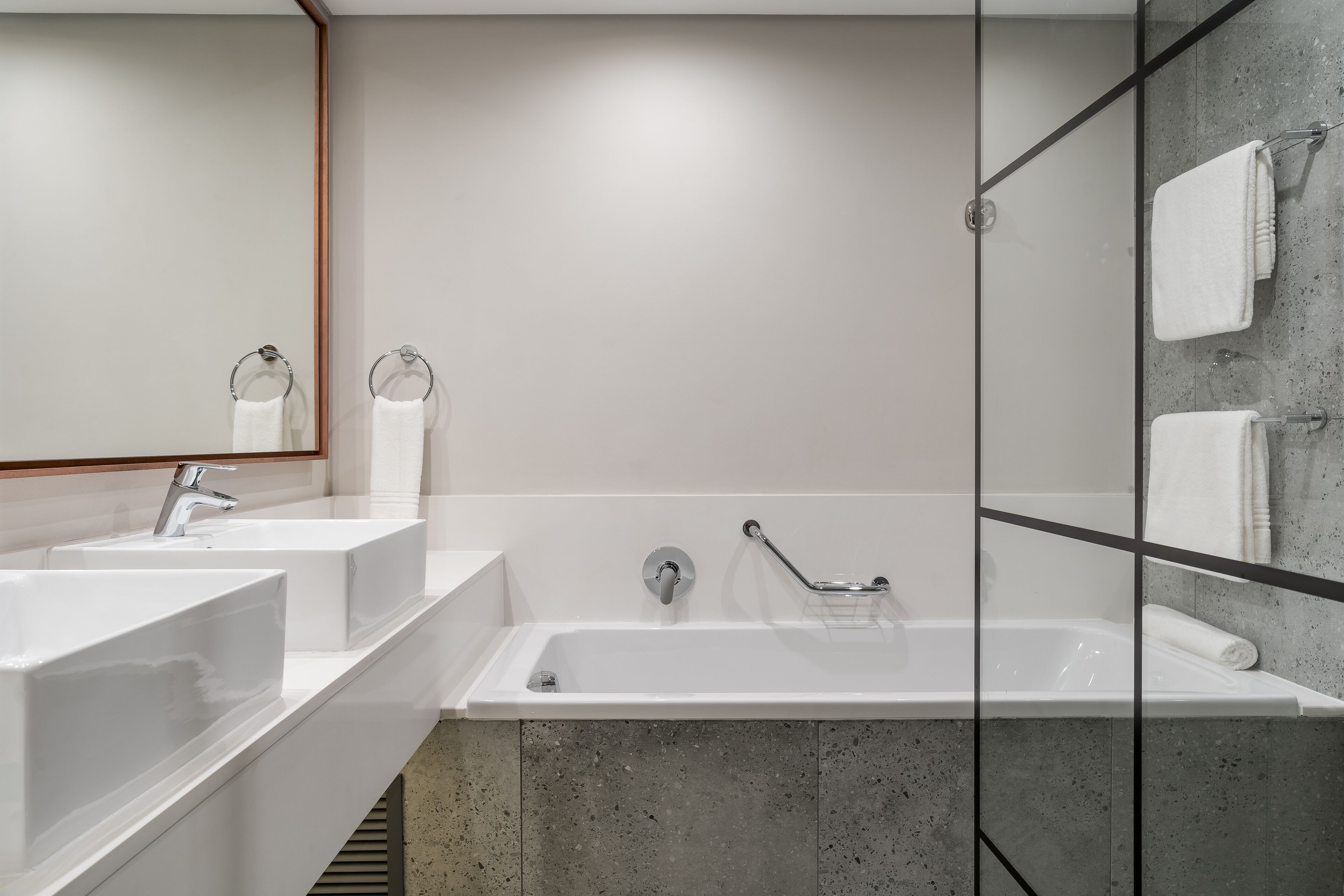 A modern bathroom with two sinks, a bathtub, and a glass shower enclosure.