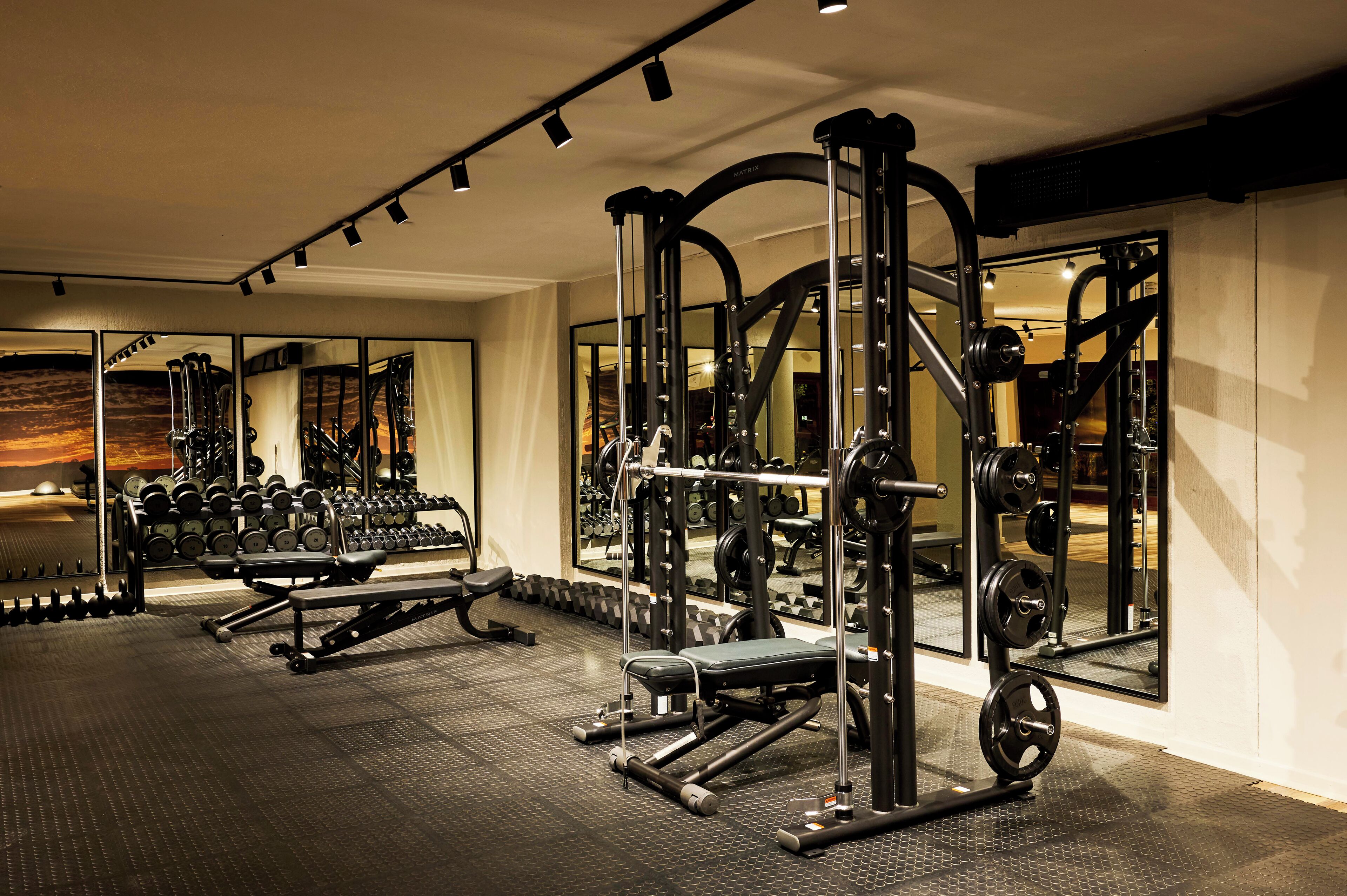 A gym with various exercise equipment, mirrors, and a wall of dumbbells.