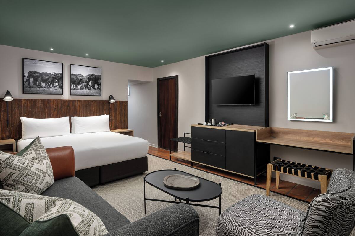 A modern hotel room with a large bed, a flat-screen TV, a desk, and a sofa.