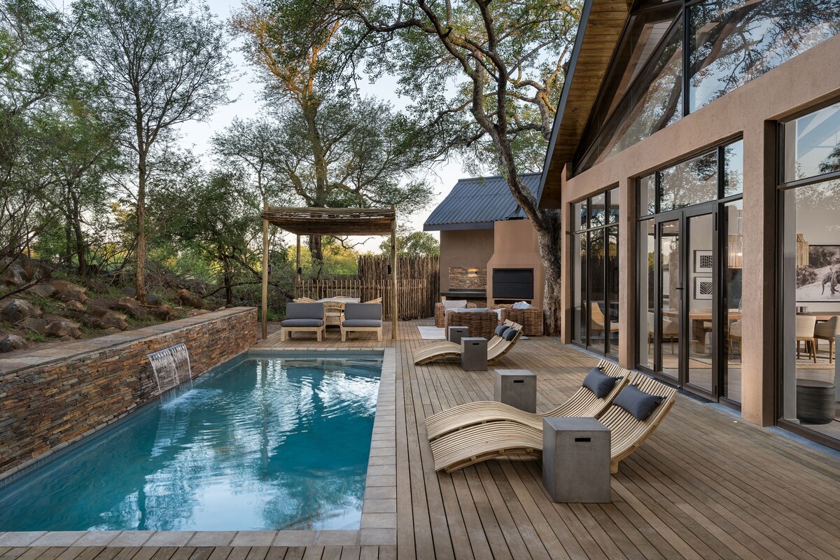 A pool area with wooden deck, lounge chairs, and a pergola.