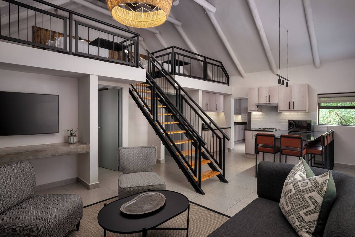 A modern loft-style apartment with a staircase connecting two floors, a dining area, and a kitchen.