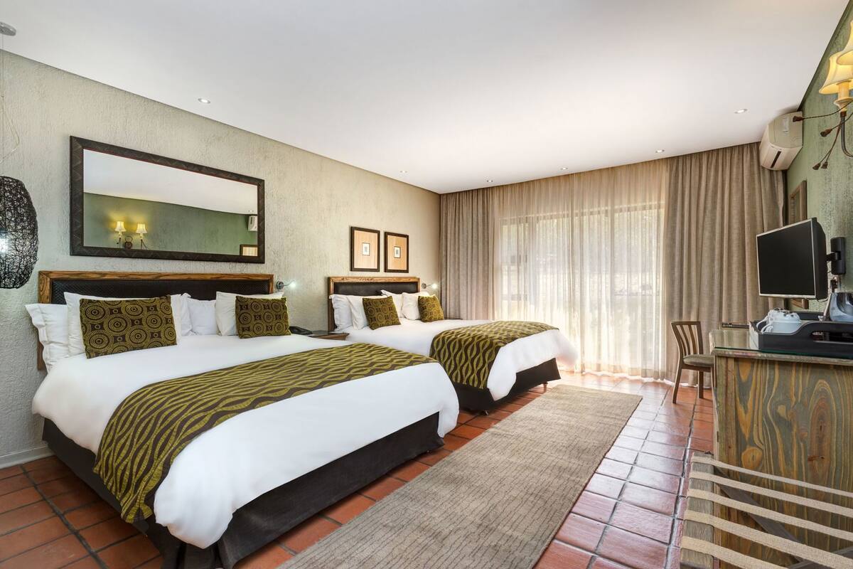 A hotel room with two beds, a desk, a television, and a large window with curtains.