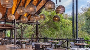 Un restaurante al aire libre con mesas redondas y sillas de mimbre, rodeado por una terraza de madera y una valla negra.