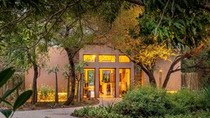 Un edificio de spa con amplios ventanales de vidrio, rodeado de exuberante vegetación y árboles.