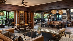 Un amplio espacio interior con sofás de cuero, una mesa de comedor y sillas de mimbre. Hay lámparas colgantes y un ventilador de techo.