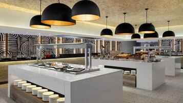 A modern buffet setup with multiple serving stations, a patterned wall design, and hanging pendant lights.