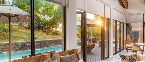 Un interior moderno con ventanas amplias que dan a una piscina, mobiliario de mimbre y una terraza de madera.
