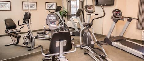 Un gimnasio con máquinas de cardio, una cinta de correr y un espejo grande.