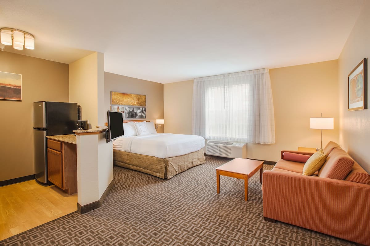 A hotel room with a bed, a sofa, a desk with a television, a window with curtains, and a patterned carpet.