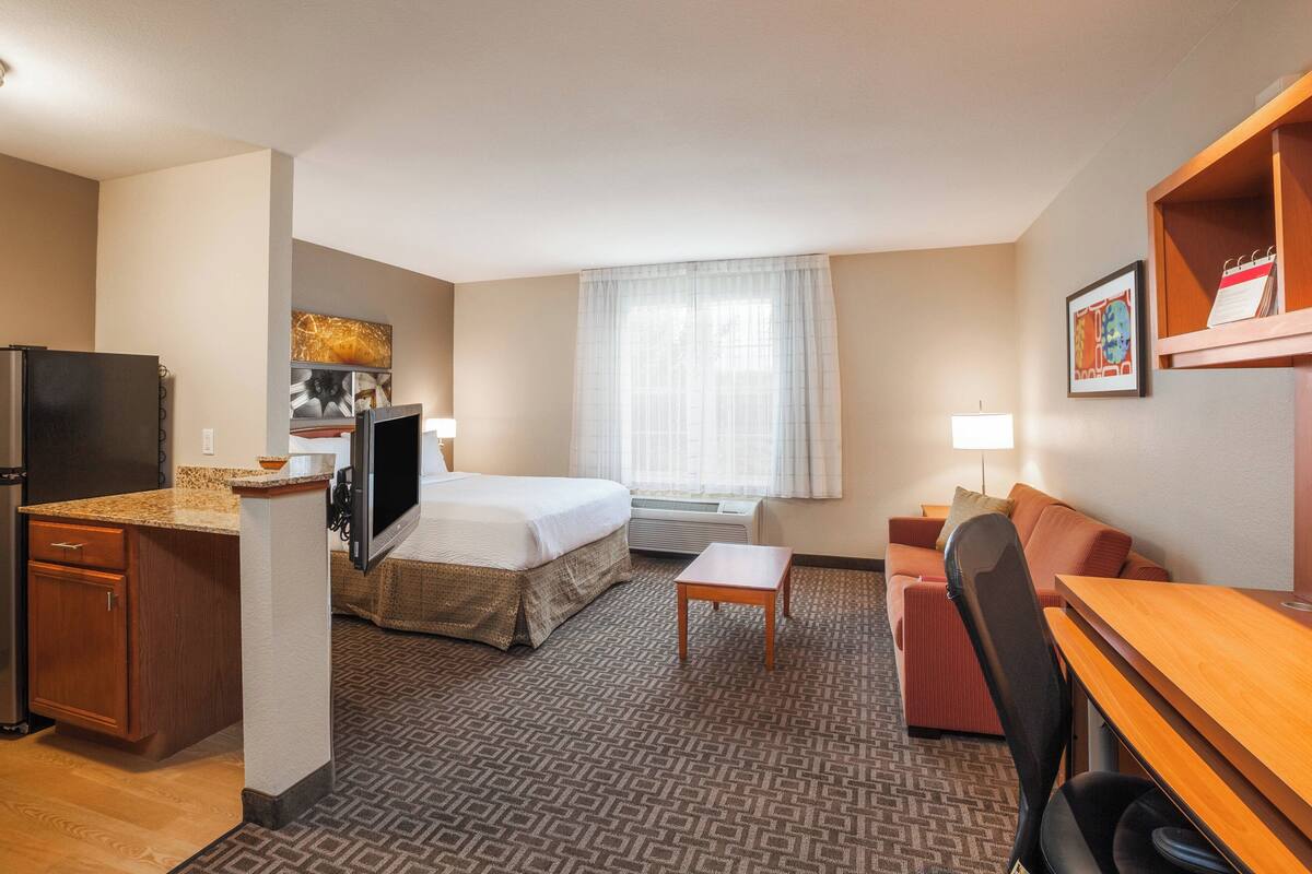 A hotel room with a bed, a desk, a chair, a TV, and a window with curtains.