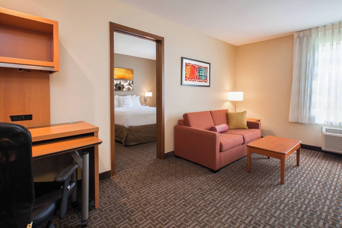 A hotel room with a desk, a sofa, a bed, and a window with curtains.