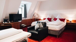 A hotel room with a bed, a desk with a TV, a chair, and a small table. - Hotel Amberger (Würzburg)