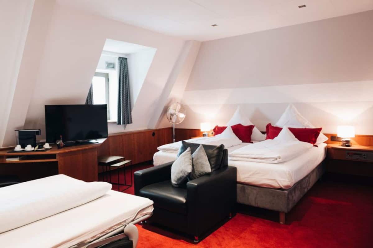 A hotel room with a bed, a desk with a TV, a chair, and a small table.