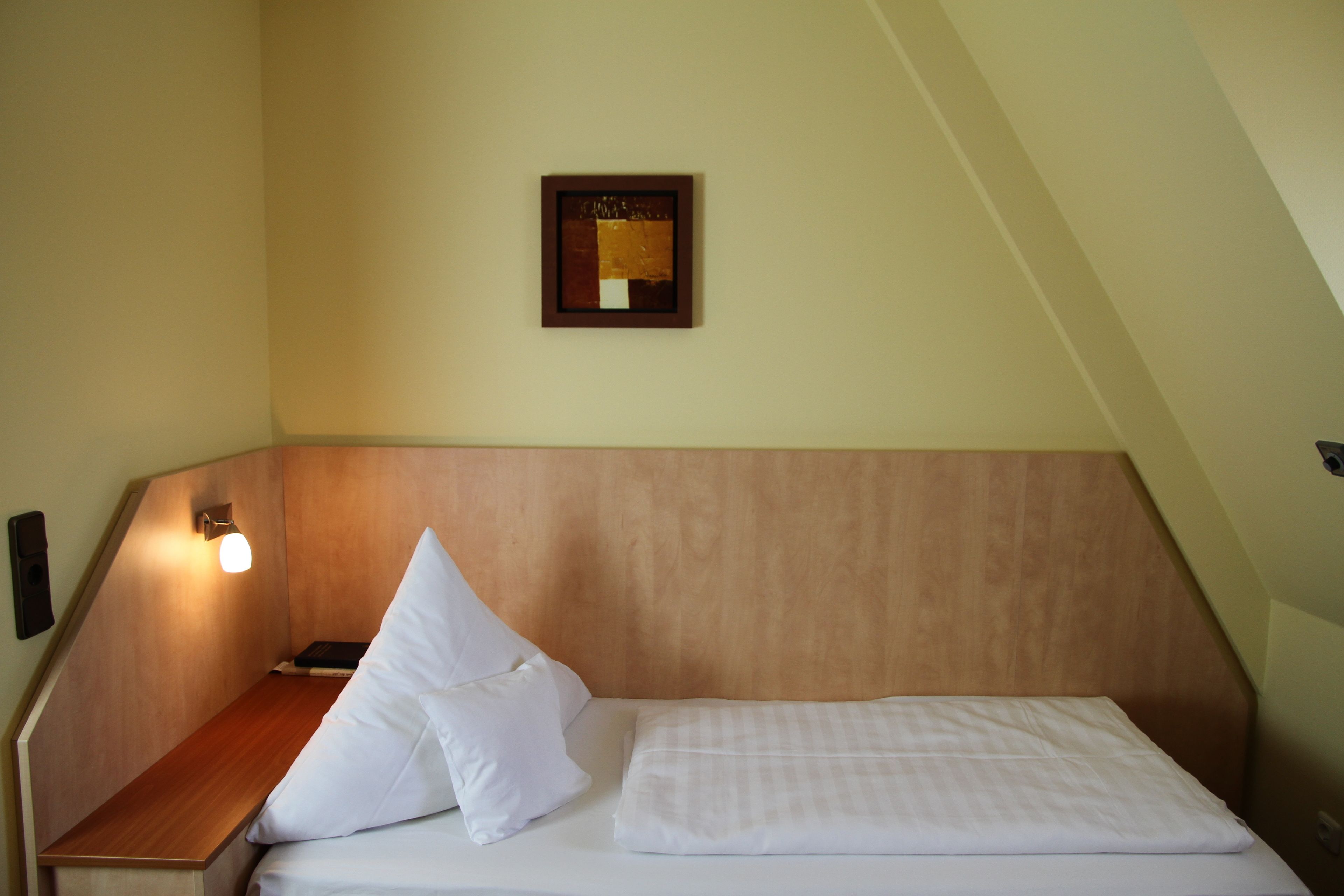 Una cama bien hecha con sábanas blancas en una habitación con techo inclinado y cabecera de madera.