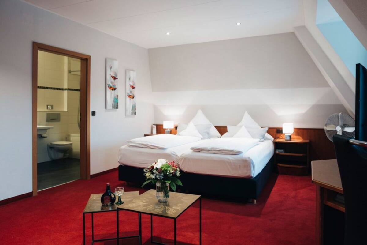 A hotel room with a large bed, two bedside tables with lamps, a small table with a vase of flowers, and a TV on a stand.