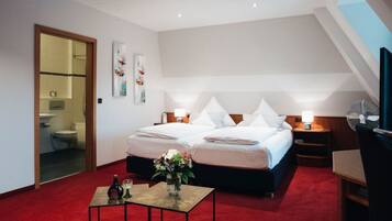 Ein Hotelzimmer mit einem großen Bett, zwei Nachttischen mit Lampen, einem kleinen Tisch mit Blumenvase und einem Fernseher auf einem Schrank.