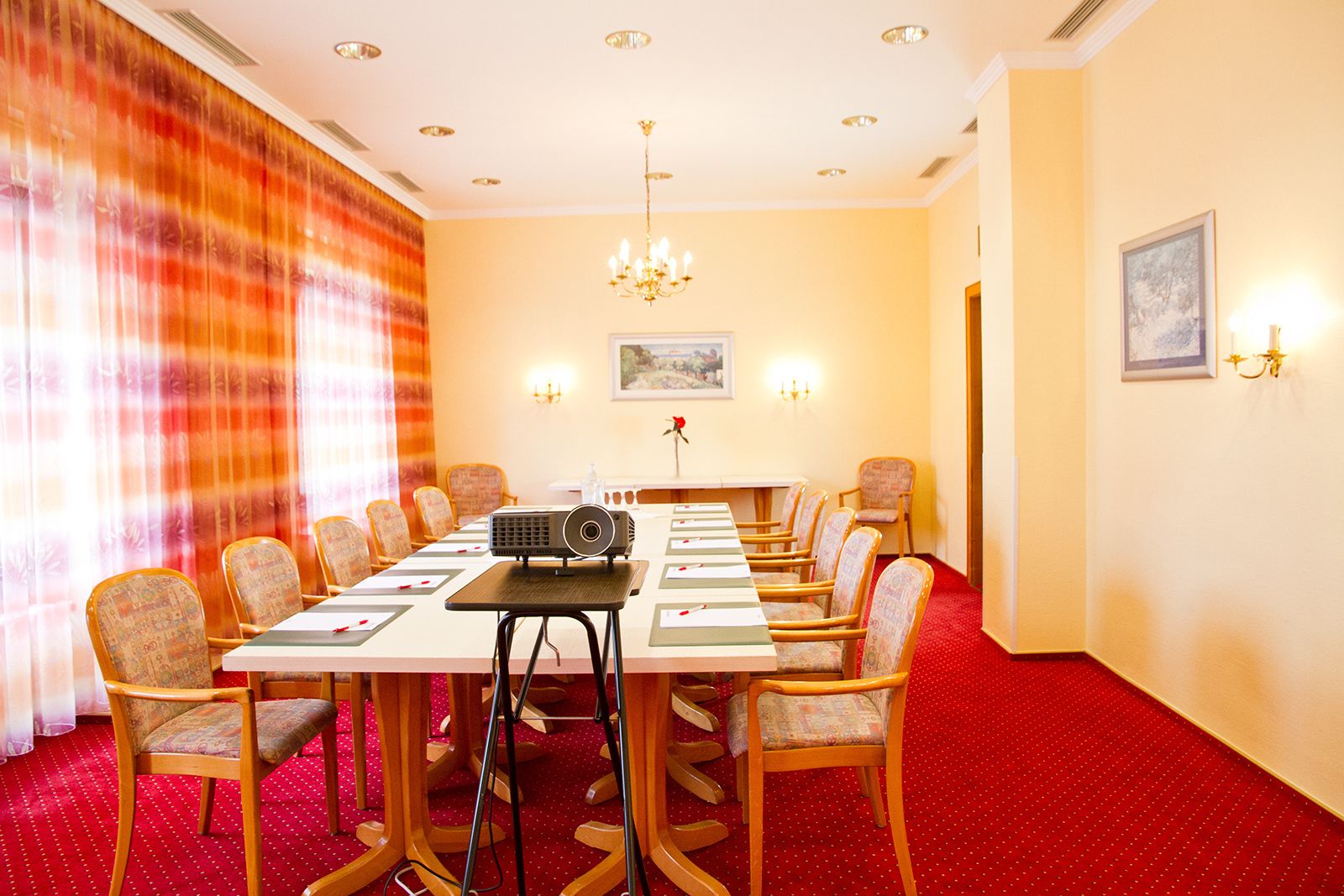 A conference room with a long table, chairs, a projector, and a red carpet.