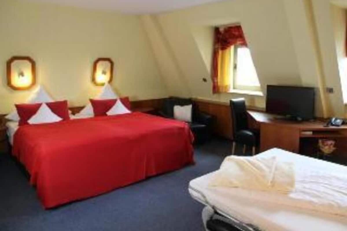 A hotel room with a bed, a desk, a chair, a television, and a window with curtains.